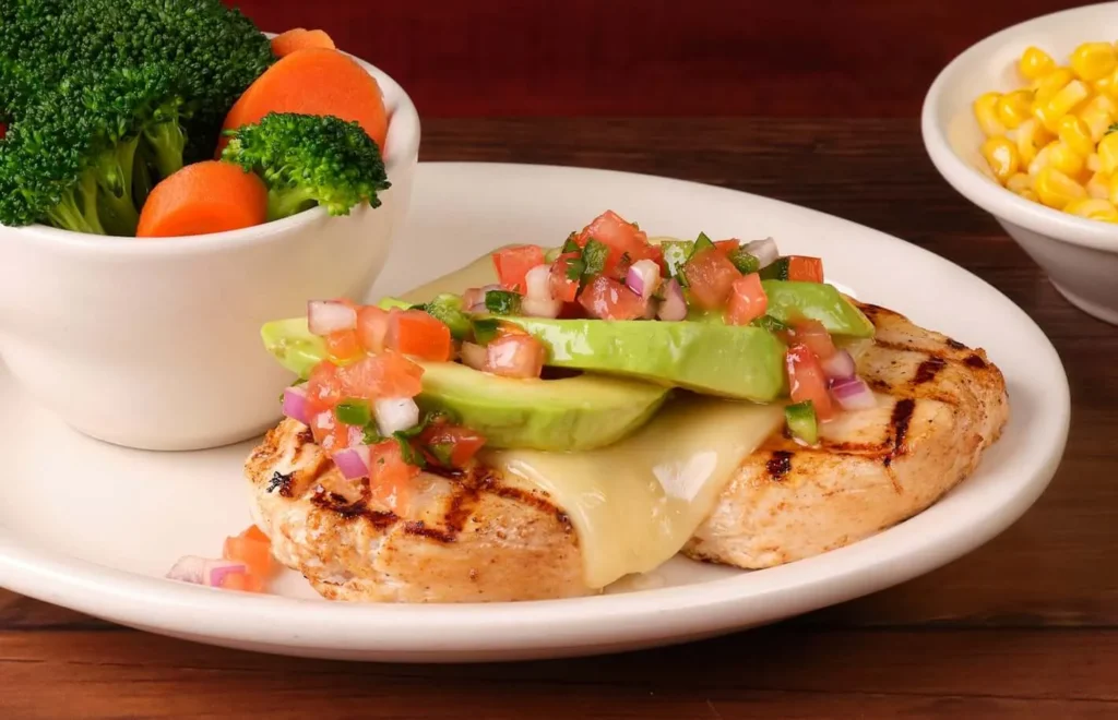 California chicken dinner with avocado slices on top served with steamed vegetables 