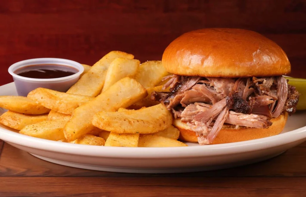 pulled pork sandwich served with sauce and fries