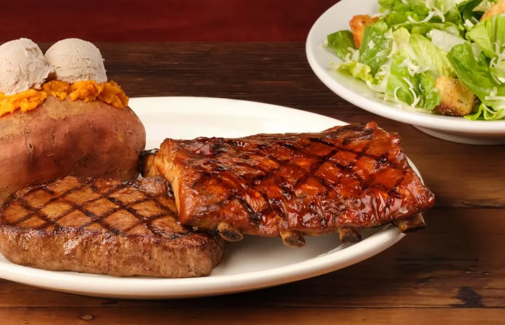 A pair of sirloin and ribs with baked potato serving on the side 
